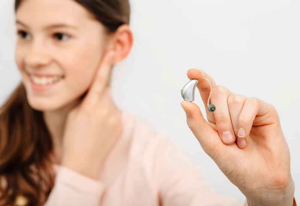 Woman with hearing aids in her hand and pointing to her ear