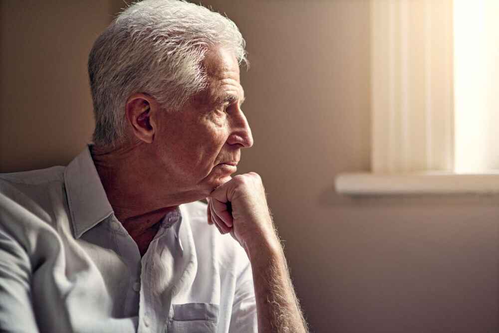 Senior man going through depression because of hearing loss and looking out window