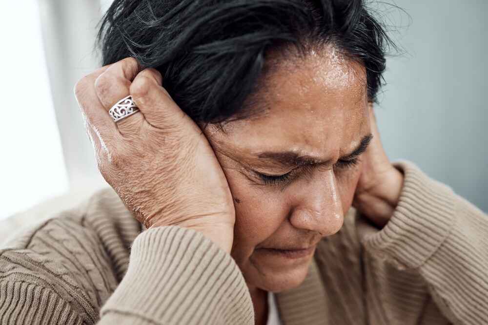 Woman closing her ears with her hands due to experiencing loud tinnitus ringing